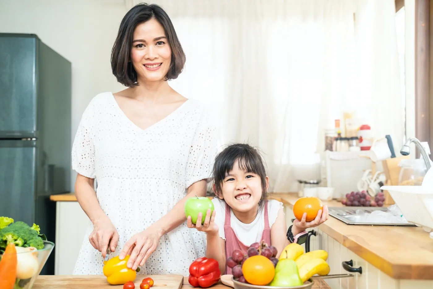 Mãe jovem preparando refeição saudável com a filha na cozinha